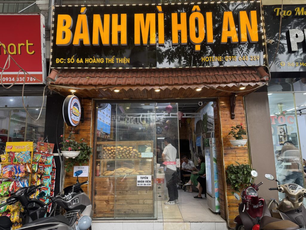 Exterior of a Vietnamese banh mi shop with signboard and motorbikes parked outside