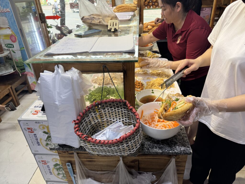 Staff preparing Vietnamese banh mi sandwich with bread, pickled vegetables, and ingredients at a shop counter