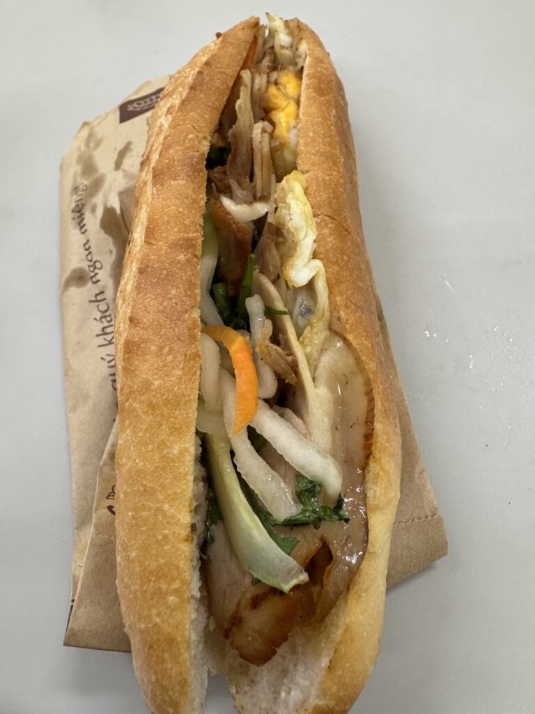 Vietnamese banh mi sandwich cut open, showing egg, sliced meat, pickled vegetables, and herbs
