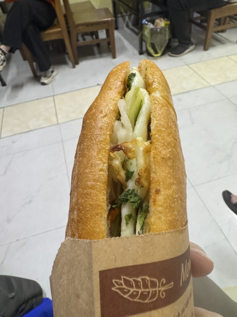 Close-up of a Vietnamese banh mi sandwich held in hand with cucumber, pickled vegetables, and herbs