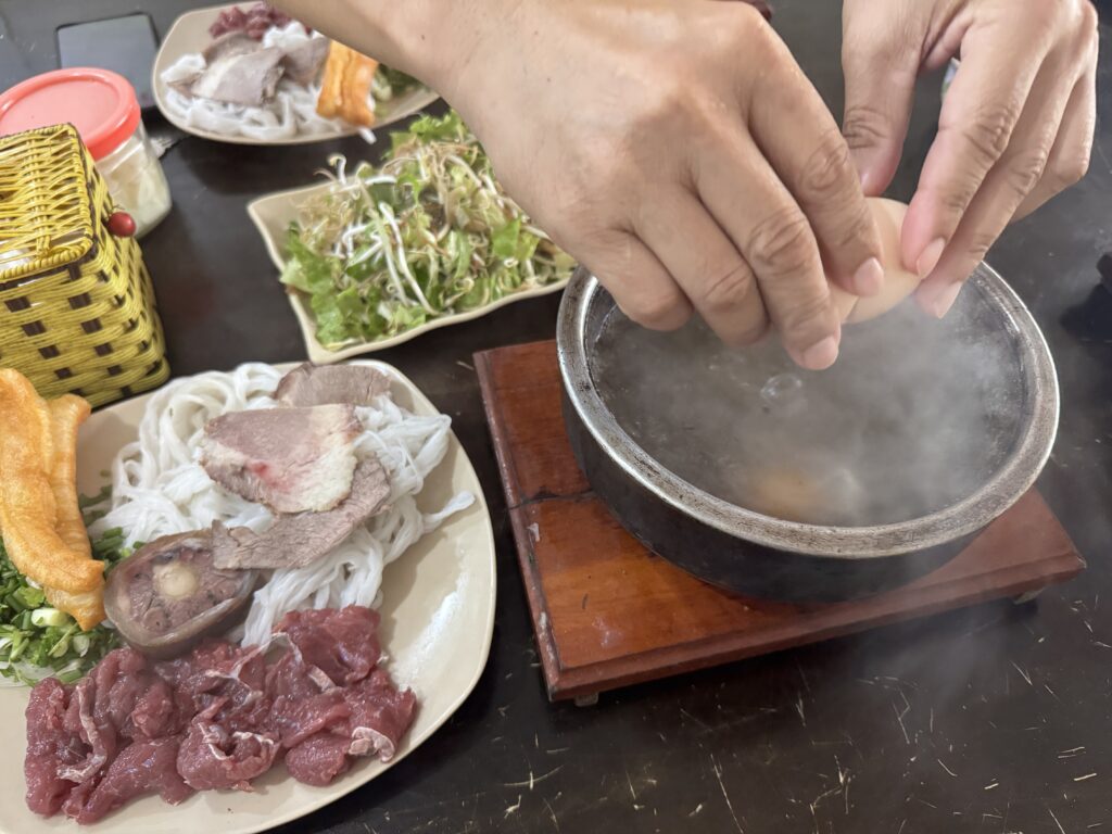 Preparing hot stone bowl water buffalo pho by adding an egg into the heated stone bowl in Hung Yen, Vietnam.